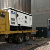 Generador eléctrico industrial SEA de color blanco con base negra montado sobre camión plataforma amarillo en zona de descarga.